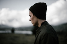 side profile of a man in a beanie standing outdoors 