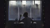 man drinking water at a desk in front of a window 