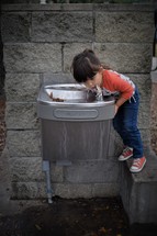 a little girl drinking from a water fountain 