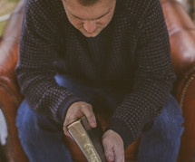 Man sitting a chair praying while holding a Bible.