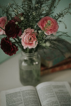 vase with red and pink flowers and an opened Bible 