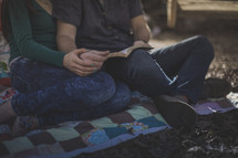A man and woman sitting on a blanket reading the Bible together