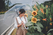 a young woman standing in a field of sunflowers holding an umbrella 