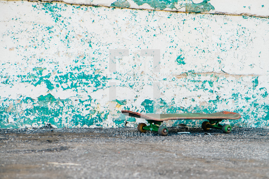 Skateboard on the pavement by a weathered wall.