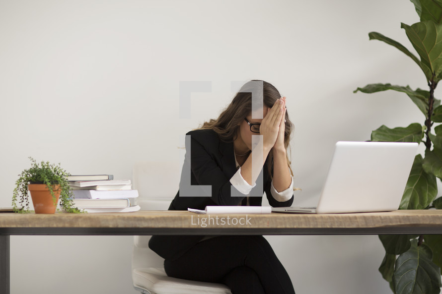 a businesswoman sitting behind a desk praying 