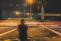 a man sitting on a city curb at night 