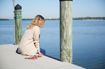 a woman sitting on a pier thinking 