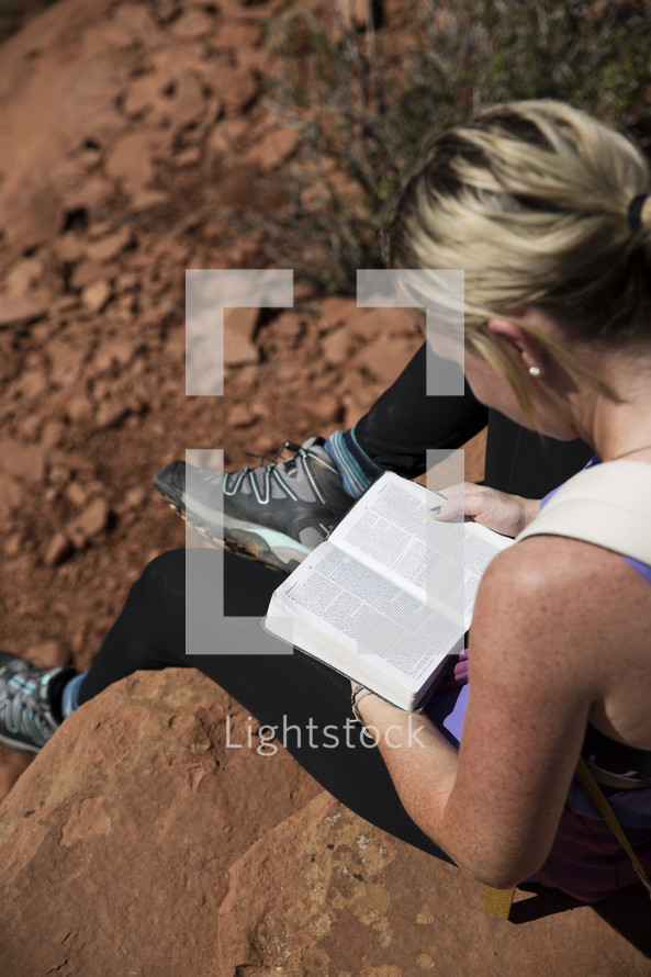 a woman sitting on a rock reading a Bible in a canyon 