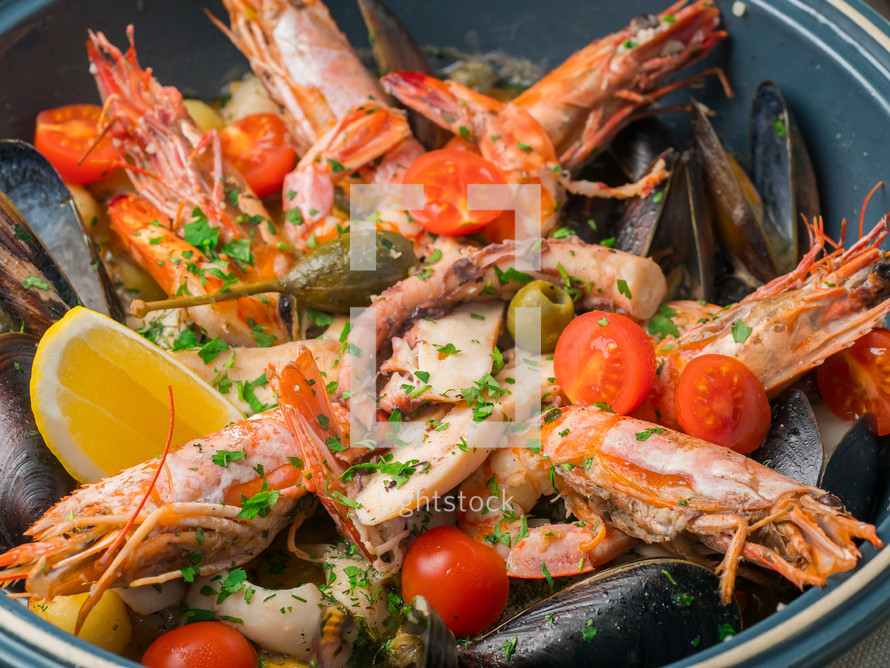 Colorful fresh seafood with vegetables and spices on blue plate in restaurant. Close up