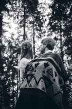 a couple wrapped in a blanket standing in a forest 