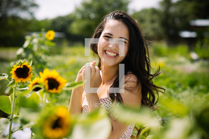 A smiling young woman in a field of sunflowers.