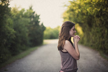 girl standing on a dirt road with praying hands 