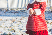 A toddler stands in the snow in winter wearing a red coat