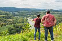 father and son looking down at a river 
