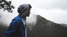 man in a hoodie looking out at a mountain 
