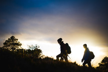 silhouettes of people hiking up a mountainside 