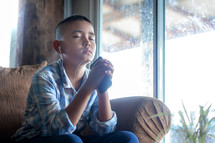 Boy praying on sofa and holding phone in hand, Listening to the voice of God,