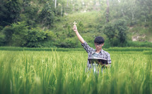 A young man in a rice field with raised hand praying 