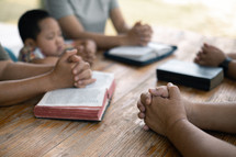 Family with young child praying at a table with bibles