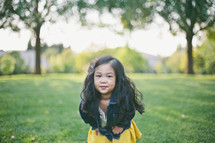 A little girl with long dark hair in a field of grass.