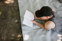 man reading a book lying on a blanket in the grass