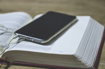 cellphone and earbuds on an open Bible 