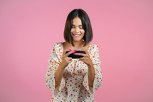 Woman playing game on smartphone on pink studio wall. Using modern technology - apps, social networks