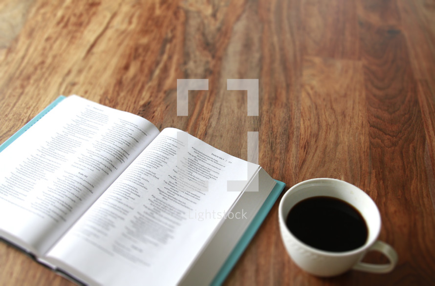 Open Bible and a white cup of coffee on a wood table