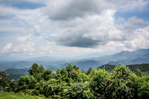 Tree-covered mountains with a cloud-filled sky.