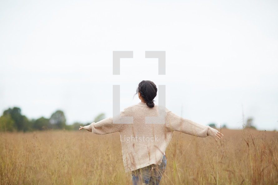 a woman with outstretched arms walking through a field 