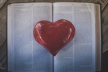 A red heart on the pages of an open Bible