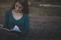 A smiling woman sitting on a bench reading the Bible