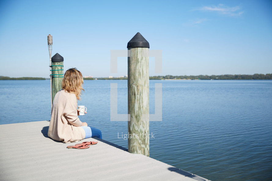 a woman sitting on a pier with coffee 