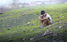 a little boy sitting on a hill praying 