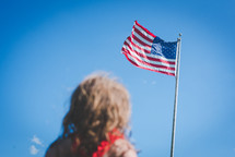 girl looking up at an American flag on a flagpole 