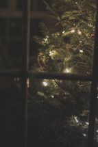 A Christmas tree with lights through a window 