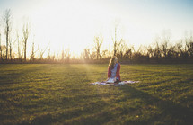 teen girl sitting on a blanket in the grass holding a Bible