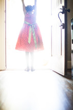 a little girl in a red dress standing in the light from an open doorway