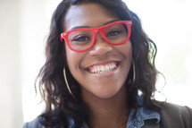 a smiling young woman in red reading glasses 