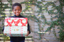 a boy child holding stacked Christmas gifts 