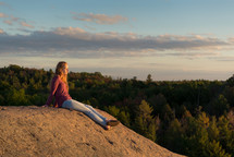 teen girl sitting on a rock on a mountaintop taking in the view 
