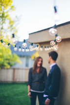 Blurry shot of a couple outdoors, standing under a string of lights 