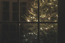 A lighted Christmas tree through a window 