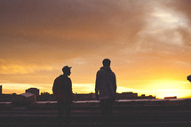 Two young men on city rooftop at sunset.