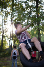 Teen boy swinging on a tire suspended from a tree.