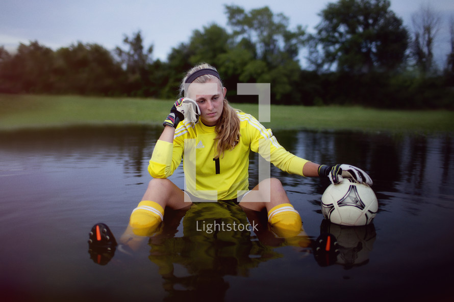 Girl sitting in a pool of water with a soccer ball.