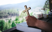 hands holding a cross on a Bible in prayer 