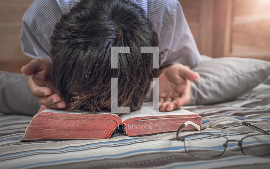 praying hands on a Bible kneeling at a bed 