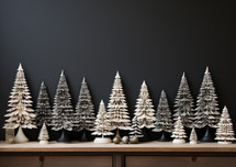 A row of snow-covered pine trees pieces on a shelf with a dark clean background. Modern, minimal, and festive. 
