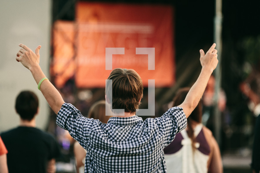 man with his hands raised in worship at an outdoor concert